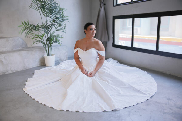 Plus-size bride siting in a white off-the-shoulder ball gown featuring a corset bodice and flowing skirt
