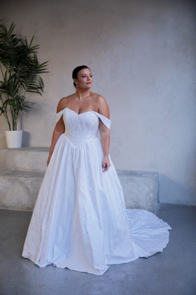 Plus-size bride in a white off-the-shoulder ball gown featuring a corset bodice and flowing skirt