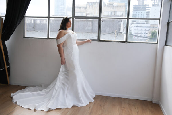 Plus-size bride wearing a sleek off-the-shoulder satin mermaid wedding gown with a corset bodice