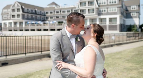 A tender moment shared between the couple against the backdrop of a stunning seaside venue. The bride’s lace gown and the groom’s gray suit create a timeless look of elegance and romance