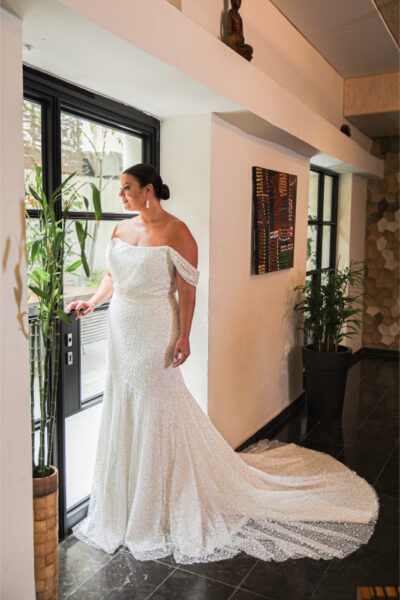 Beautiful plus-size wedding dress designed for a plus-size bride, featuring a fitted silhouette adorned with shimmering sequins and a flowing train. The gown showcases an off-the-shoulder neckline