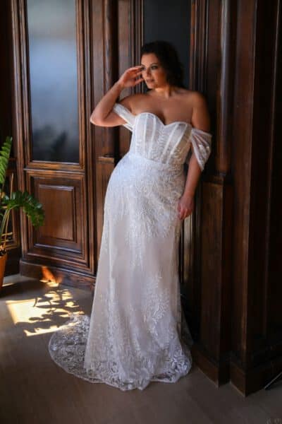 Plus-size bride in an off-the-shoulder wedding gown featuring a structured corset bodice and intricate lace details.
