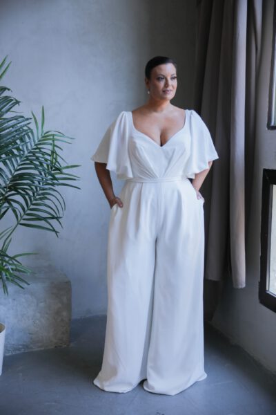 Plus-size bride in a modern white bridal jumpsuit with a deep V-neckline and wide-leg pants and flatter sleeves