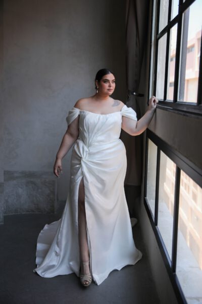 Plus-size bride in an off-the-shoulder satin wedding gown with a ruched bodice and thigh-high slit