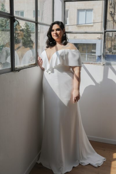 Plus-size bride in an elegant off-the-shoulder wedding gown with a deep V-neckline and fitted silhouette
