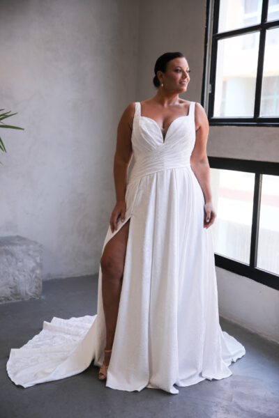 Plus-size bride in a sleeveless V-neck wedding gown with a high slit and ruched bodice, offering a modern and sophisticated look