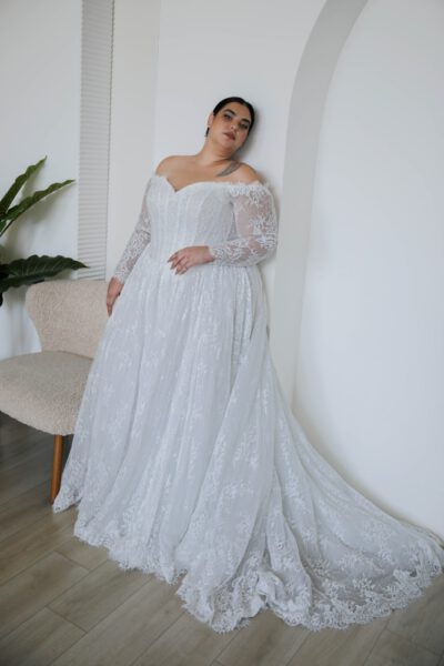Plus size Bride in flowing lace gown with long sleeves .