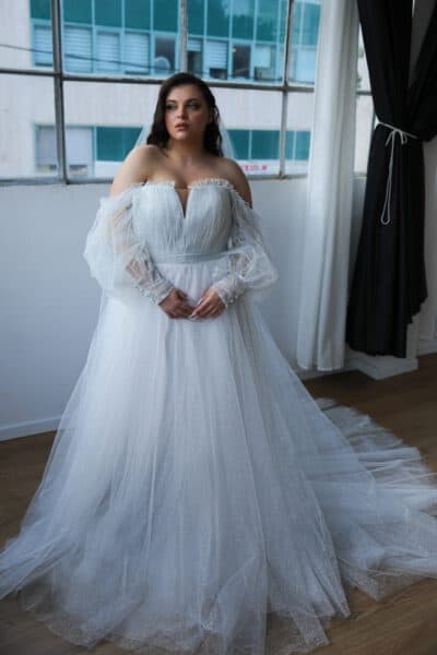 Plus-size bride in a shimmering ball gown with off-the-shoulder long sleeves and a deep V-neckline