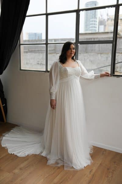 Plus-size bride in a chiffon wedding gown with long sheer sleeves, a square neckline, and flowing skirt