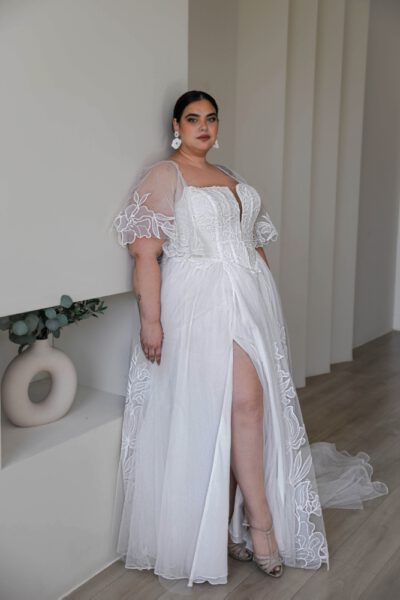 Plus-size bride in a lace wedding gown with puff sleeves, square neckline, and a thigh-high slit, blending modern style with romantic details.