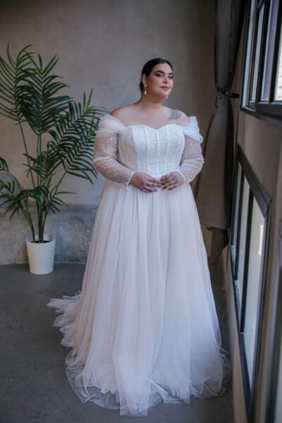 Plus-size bride in an off-the-shoulder tulle wedding gown with sheer long sleeves and intricate beaded bodice