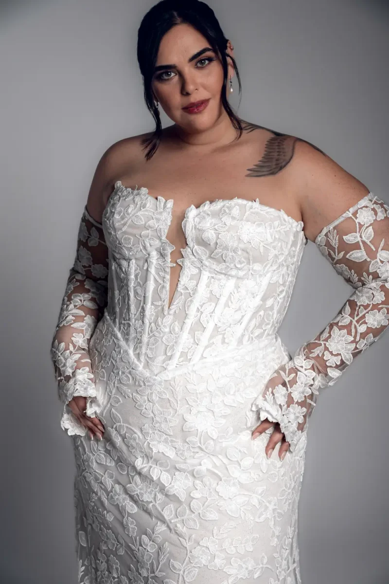 Studio Levana Corinne plus size lace fitted wedding dress with floral lace and an off-the-shoulder neckline, close-up detail