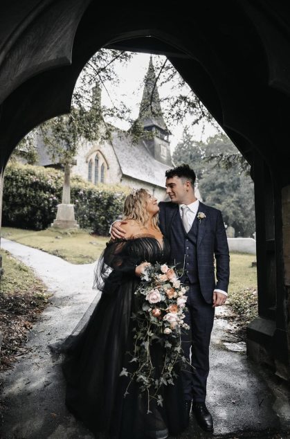 Couple with flowers posing under archway near church